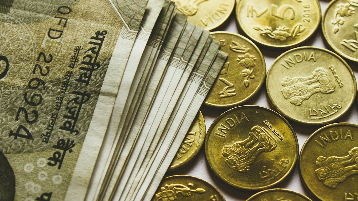 सोने के रंग के रुपये के सिक्कों के ढेर के पास फैले भारतीय रुपये के नोट