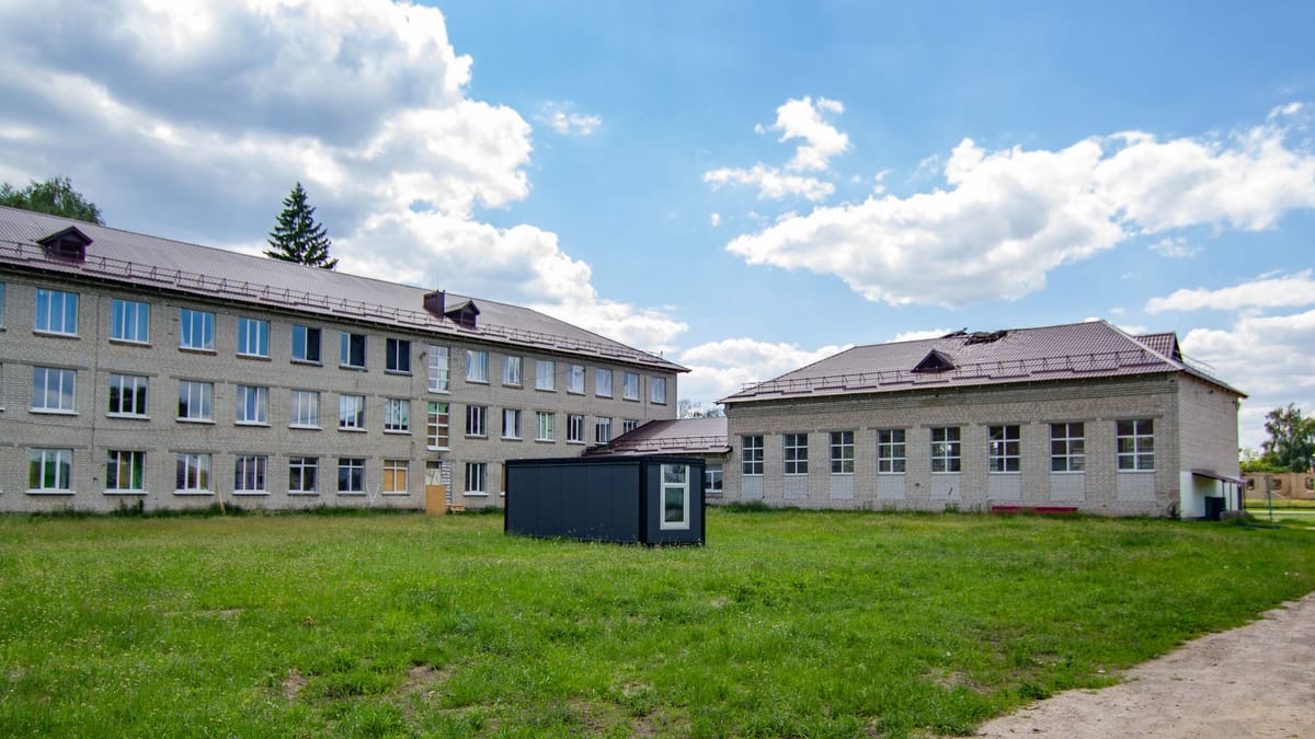 Three-storey school buildings beside a green lawn under a blue sky