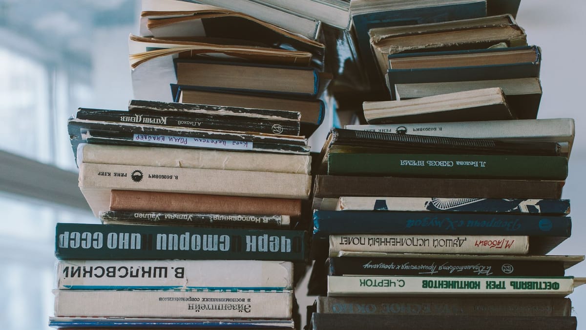A tall, uneven pile of books on a table
