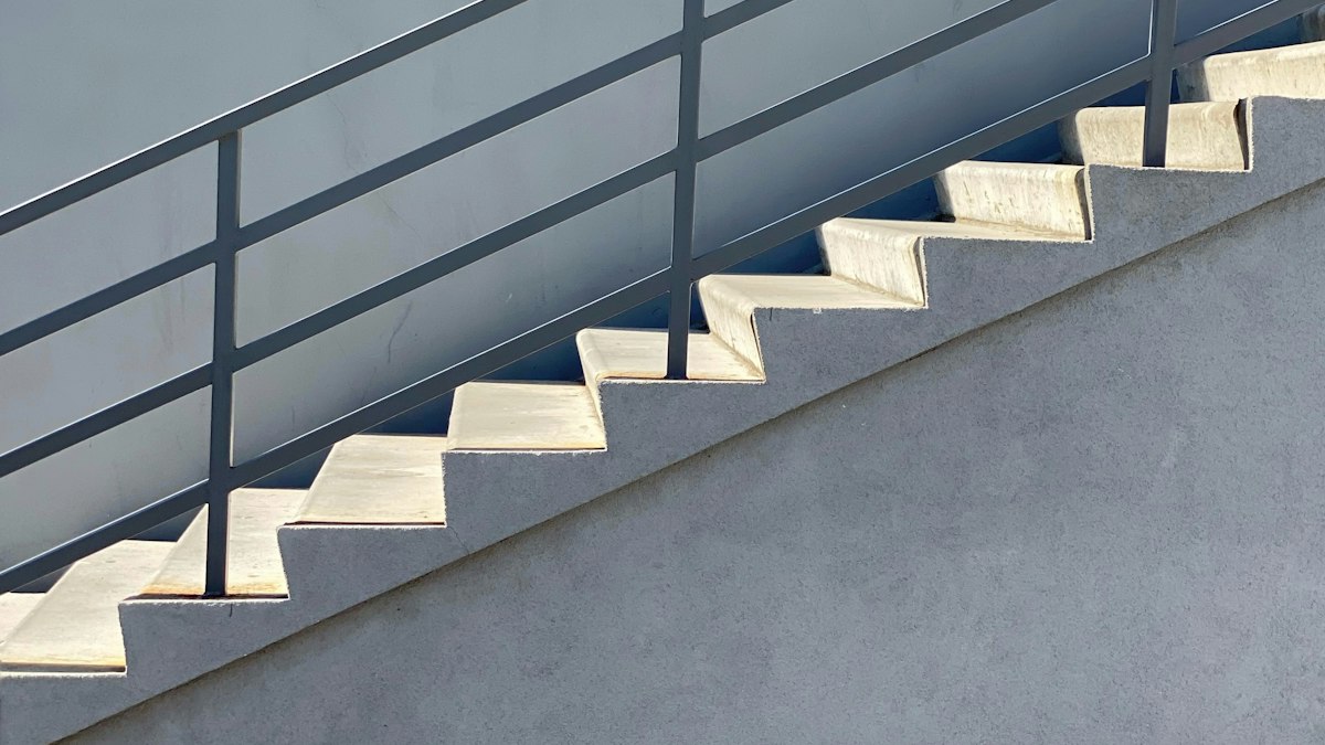A concrete staircase with a metal railing climbing along a grey wall